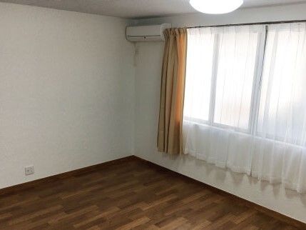 レースカーテンとカーテンが付いた大きな窓が付いた部屋はフローリングで壁にはエアコンもある。