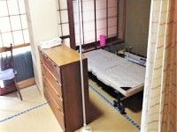 ベッドがカーテンの奥に設置され、畳の部屋の中央にタンスが置かれている。窓には障子が設置されている。