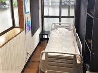 大きな窓が二つ付いたフローリングの居室には介護ベッドが置かれ、寝具もセットされている。