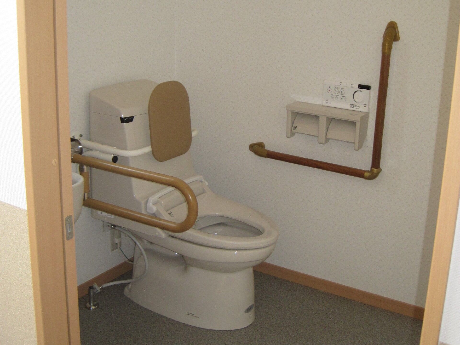 背もたれや手すりが付いたトイレの便座にふたはなく、介助スペースが広く、スライド式のドアが設置されている。