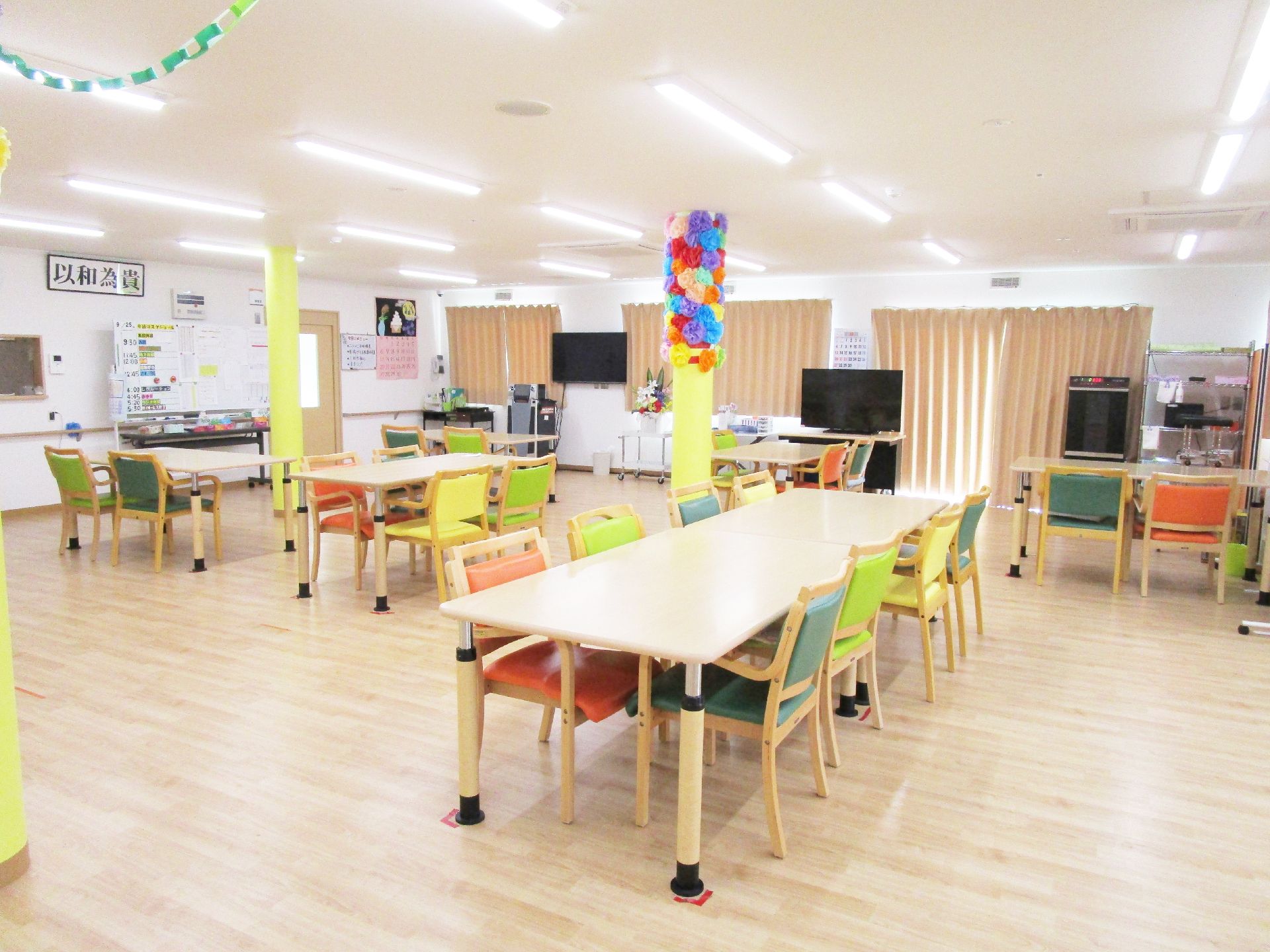 白い壁には長細い窓が二つ付き、カーテンが設置されている。部屋の中央に長細い木製のテーブルが置かれ、黄色やグリーン、オレンジの椅子がセットされている。