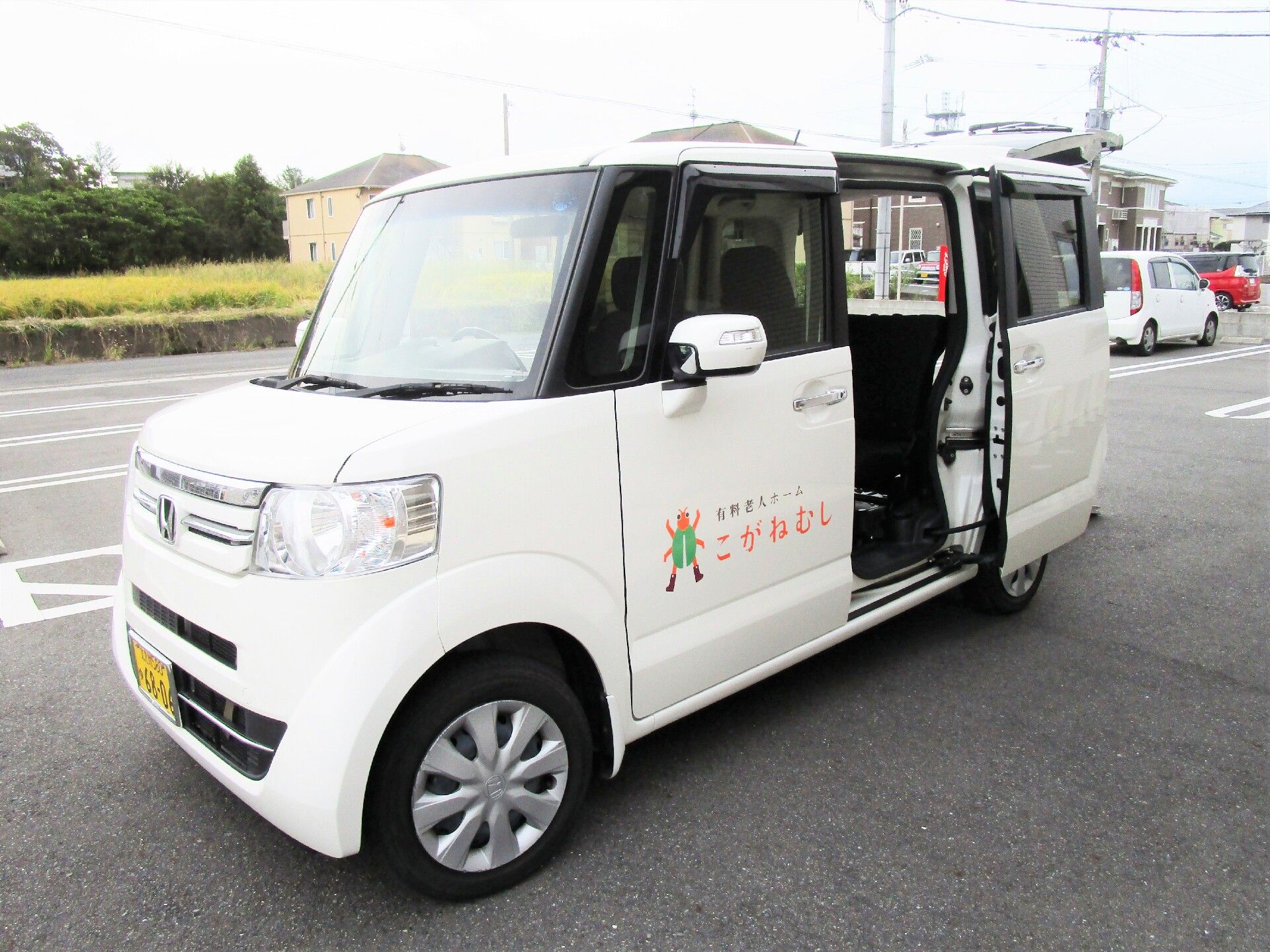 スライド式の後部座席のドアが開いている白い送迎車