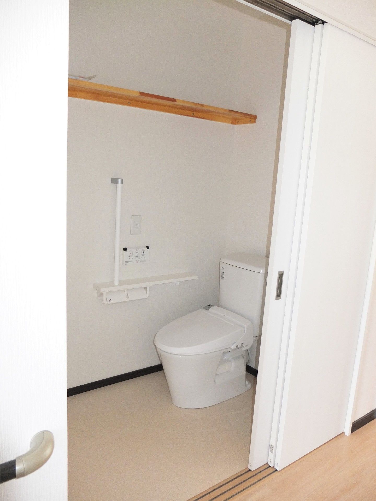 トイレは引き戸で手すりが付き、天井に近い部分には棚も付いている。