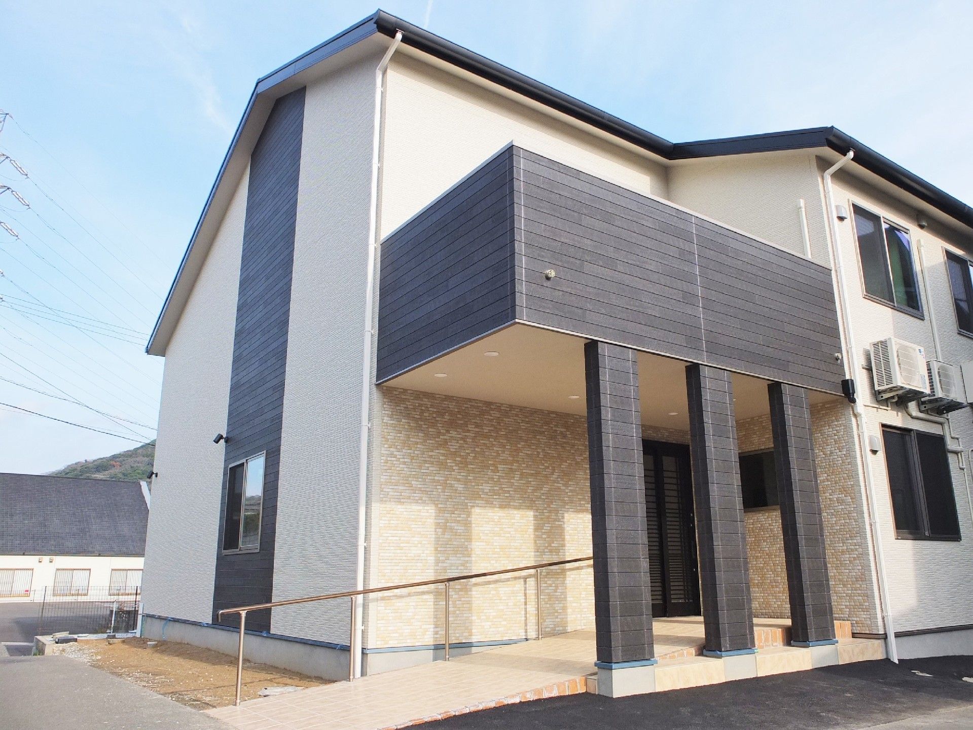 ベージュと黒の2階建ての建物。一般の住宅のような雰囲気で、玄関には手すり付きのスロープがある。