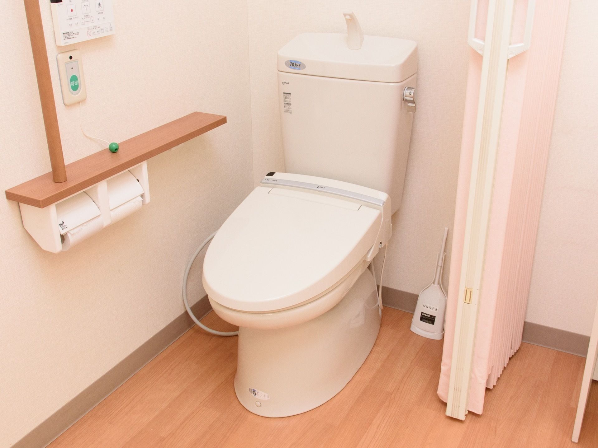 居室内にあるトイレ。仕切りはドアではなくアコーディオンカーテンが選ばれている。壁には緊急用呼び出しボタンがある。
