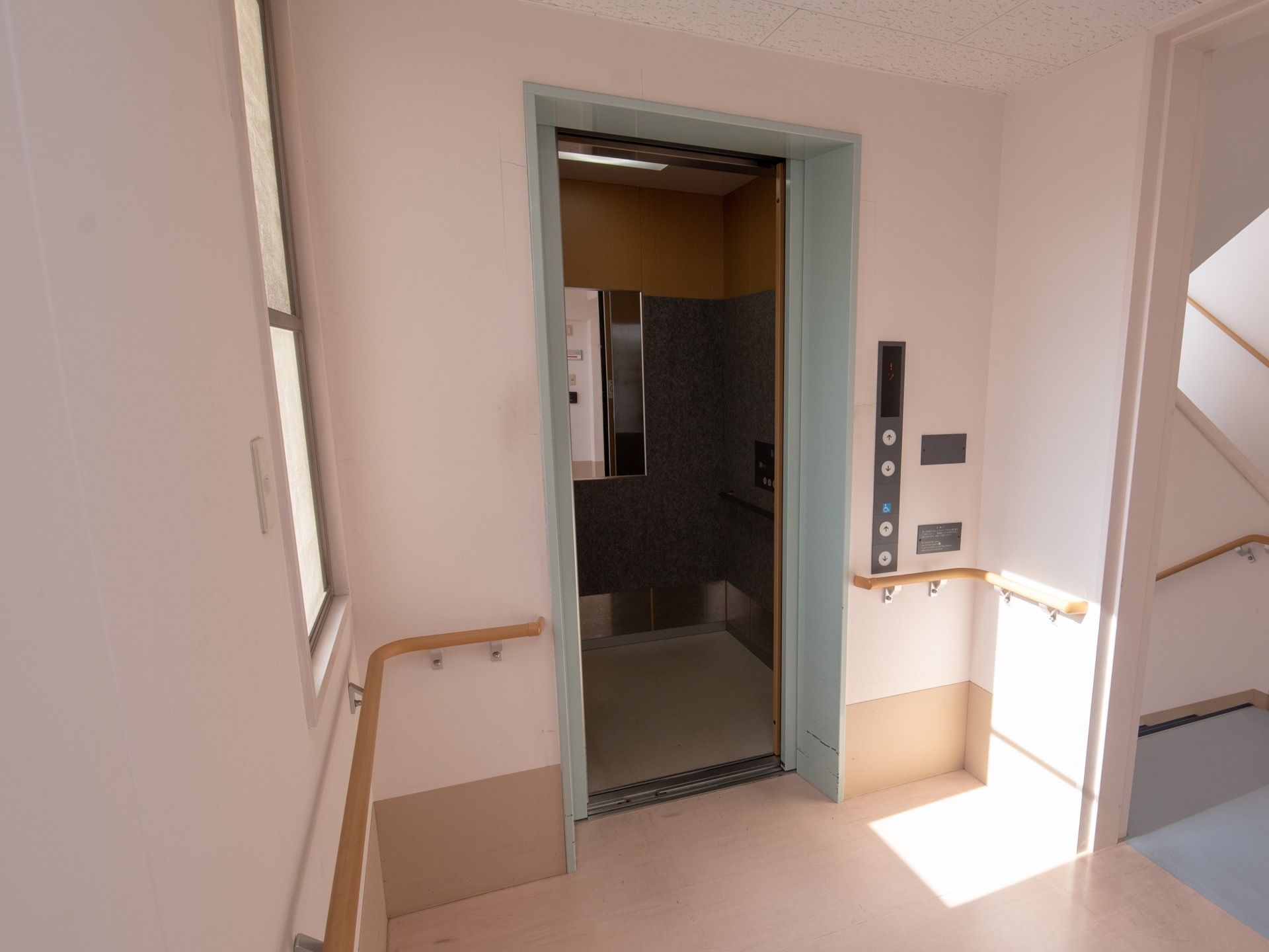 館内に完備されているエレベーターである。扉は開かれ、庫内に設置されている鏡が見える。横には、各階への階段がある。