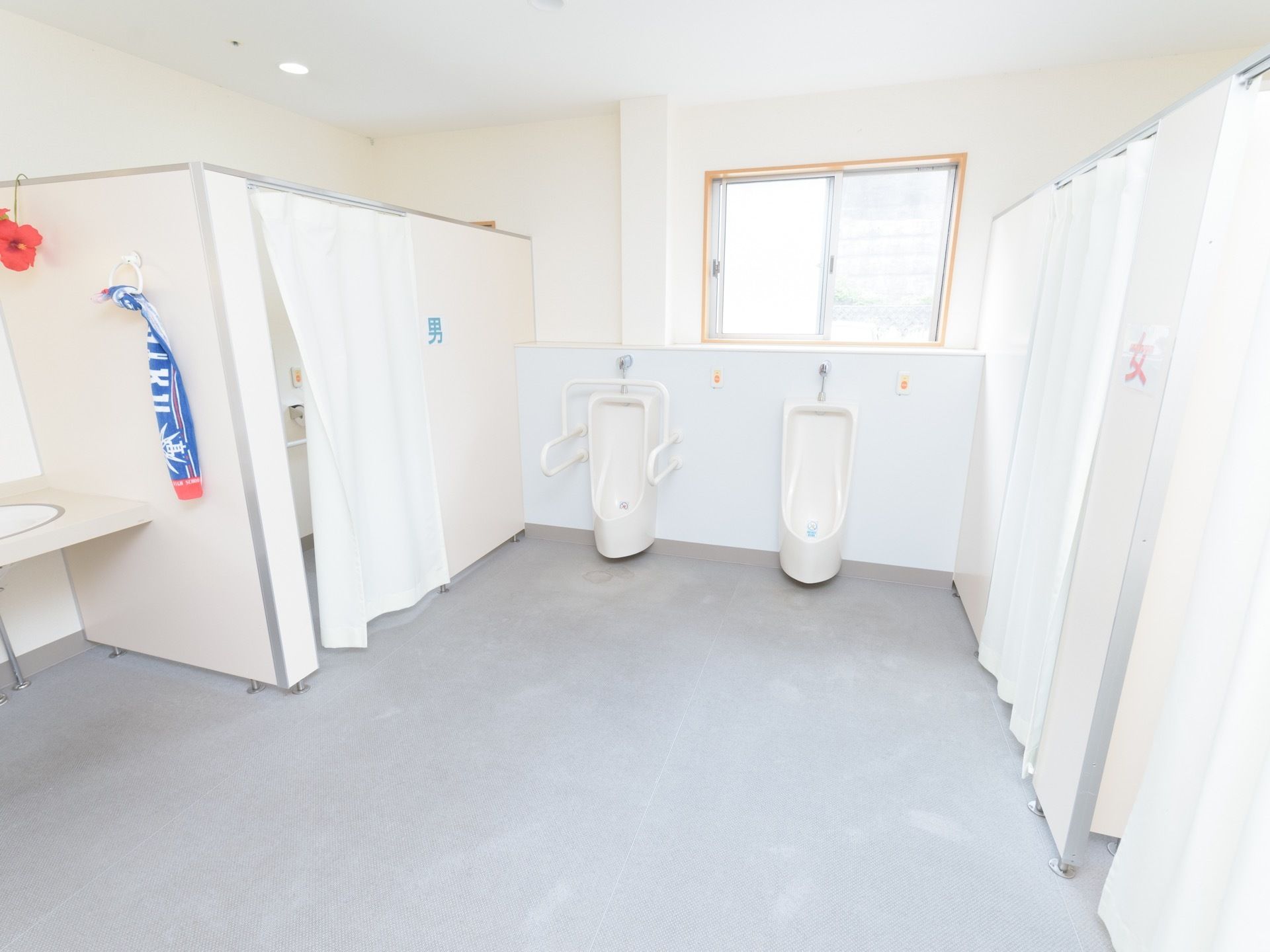 共同トイレの奥の窓際に男性用の便器が２つ並んでいる。共用トイレは白色のカーテンで仕切ることができるようになっている。