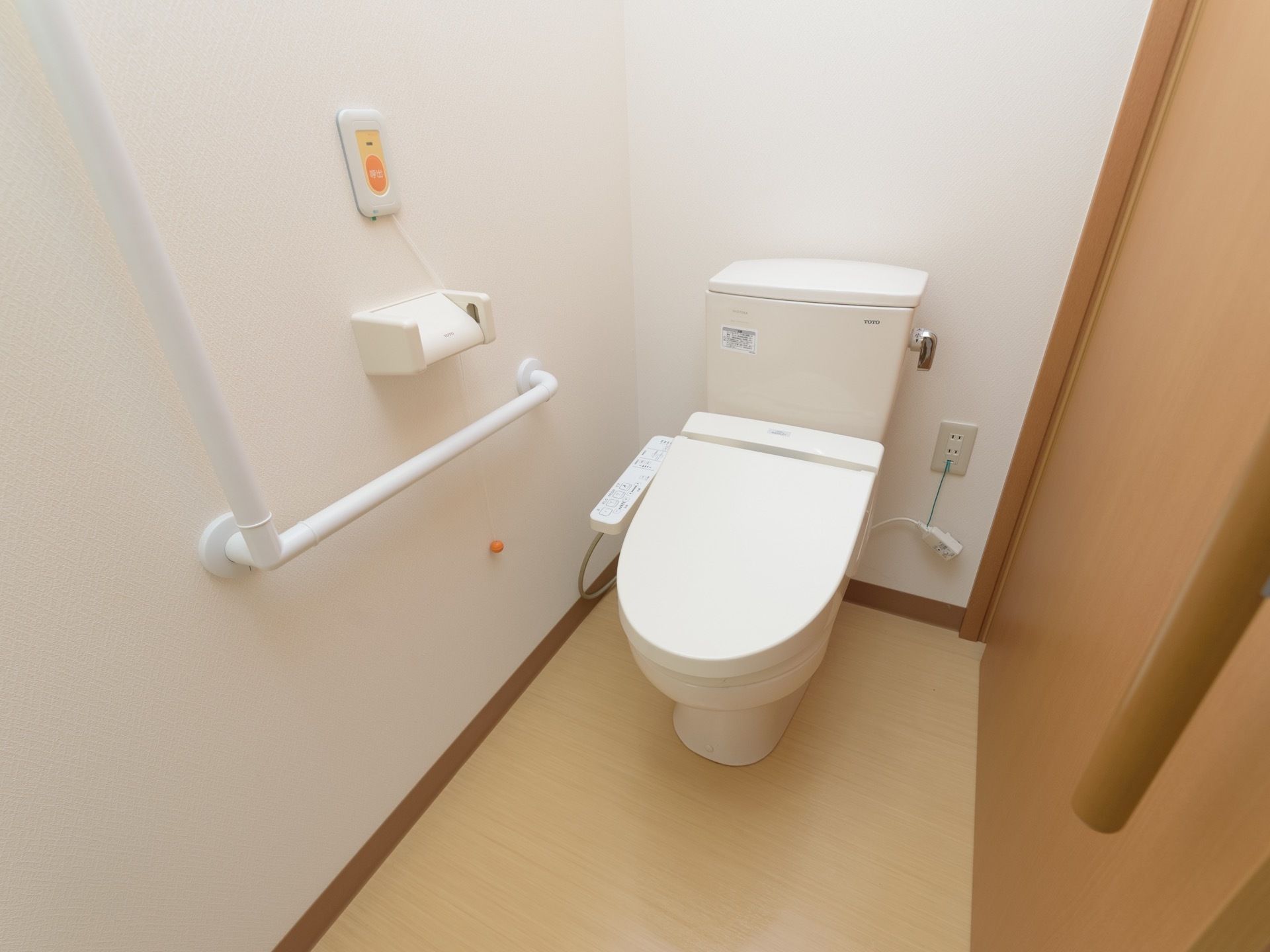 大きな取っ手がついた引き戸を開けるとトイレがある。ふたつきの便座で、壁には、縦横つながった大きな手すりが設置されている。