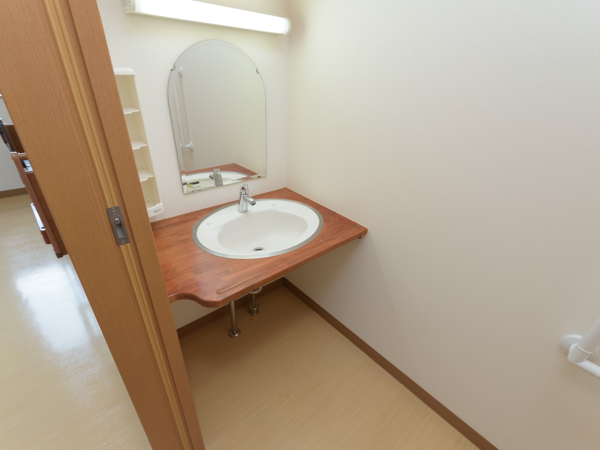 トイレの中に洗面台が設置されている。レバー式の水栓である。上部が半円形になっている鏡が前の壁に取りつけられている。