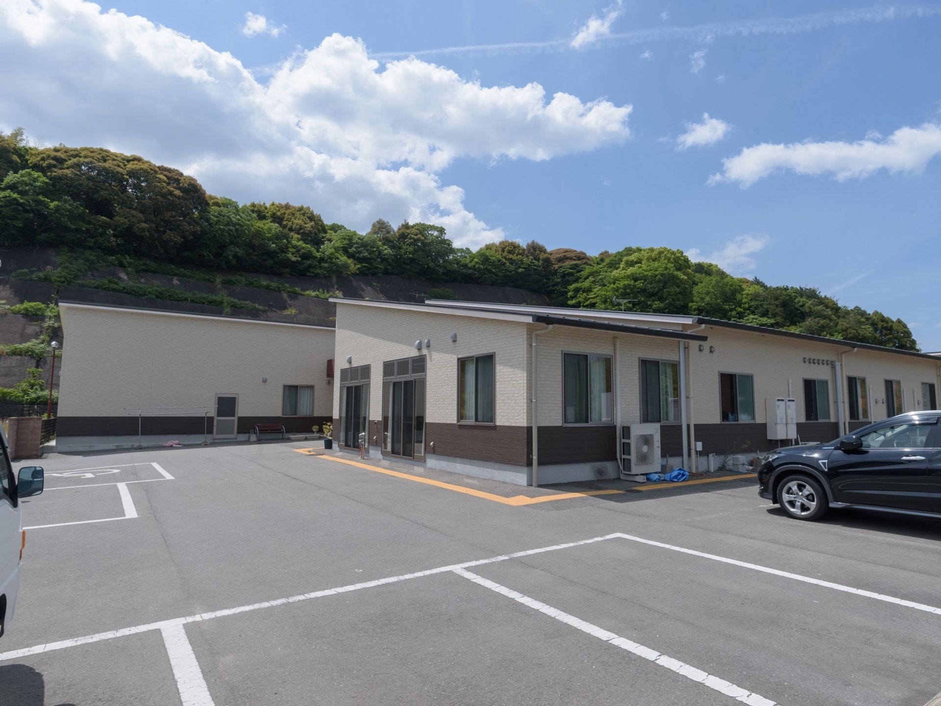 背後に小高い丘がある敷地に建っている、日当たりがとてもよい施設である。敷地内に多くの駐車スペースが確保されている。