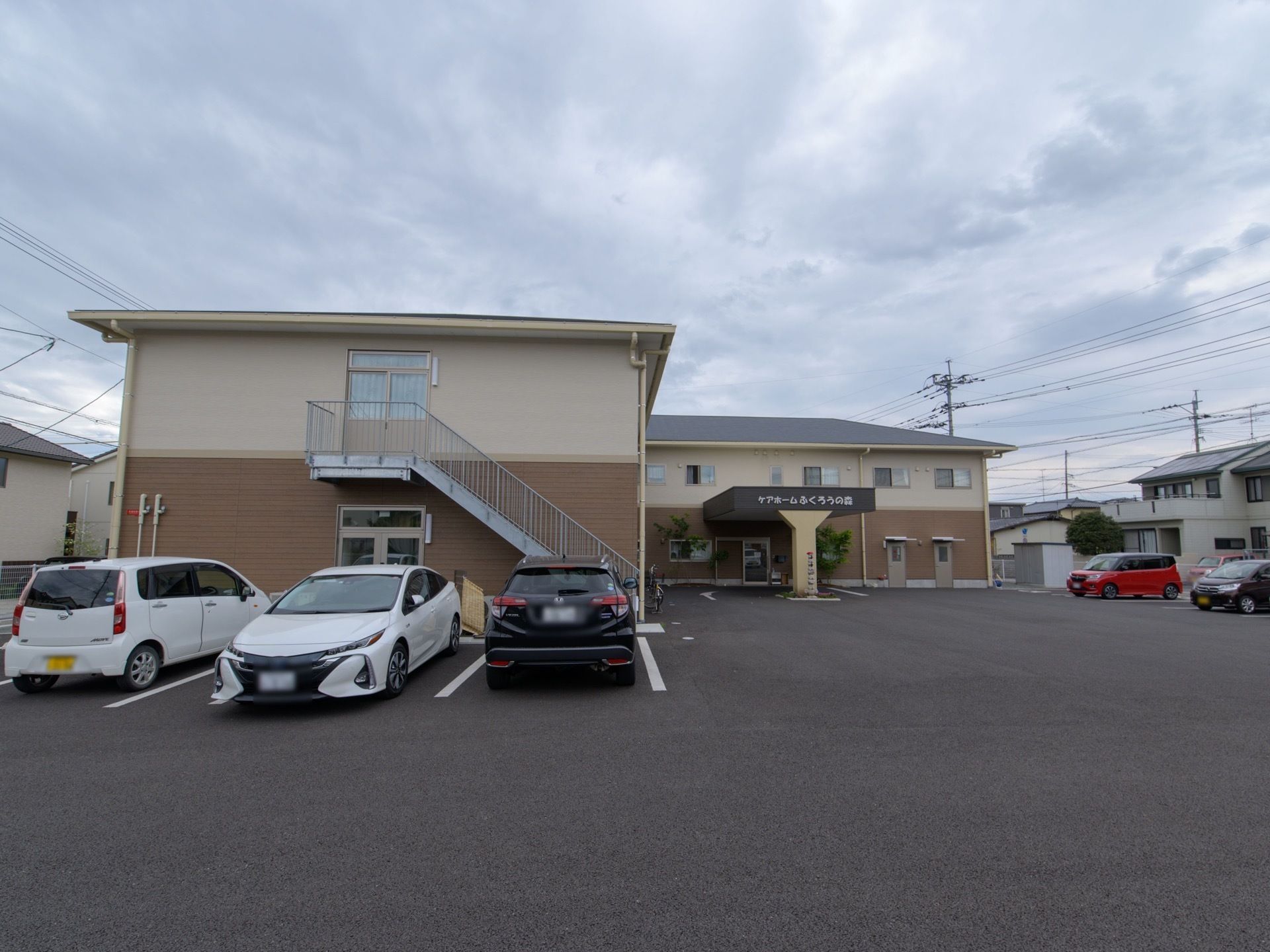 茶色の濃淡のツートンカラーの２階建ての施設である。広い敷地に建っていて、十分な駐車スペースが確保されている。