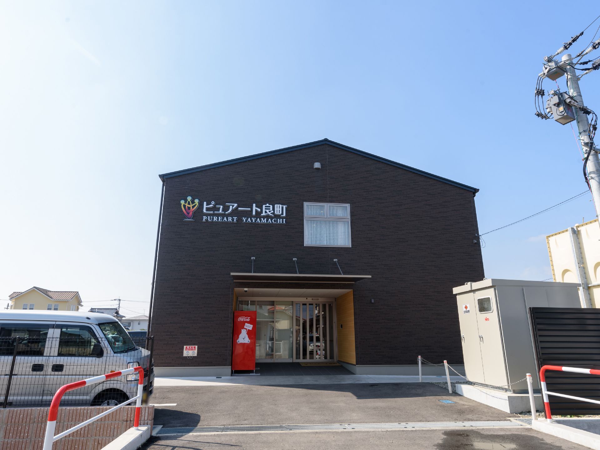 三角屋根の二階建て建物で、玄関前に自動販売機がある。二階部分の壁に、大きな文字で施設名が書かれている。