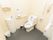 広い個室内に、洋式トイレと洗面台がある。L字型の手すりとナースコールが便器奥の壁に設置されているほか、便器脇にも可動式の手すりがある。