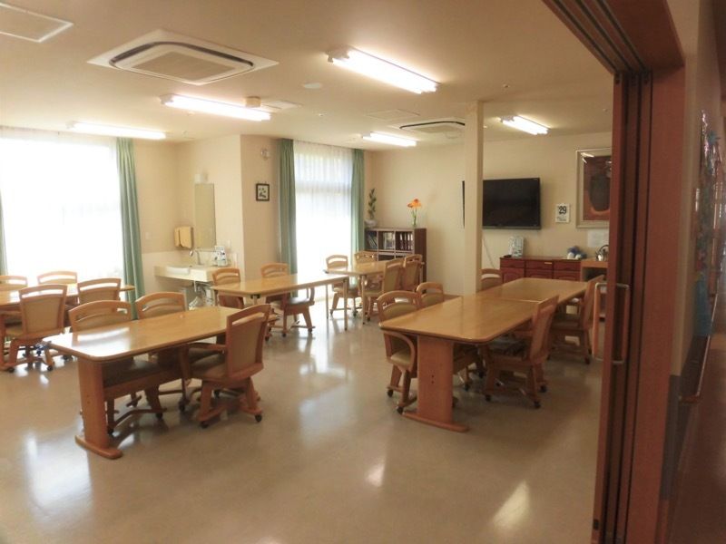 木製のダイニングテーブルが複数置かれている食堂にはテレビもあり、カーテンが付いた窓もある。