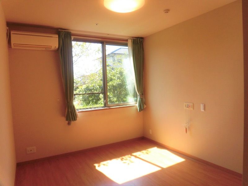 日当たりのいいフローリングの部屋。カーテン付きの窓やエアコン、緊急通報装置がある。
