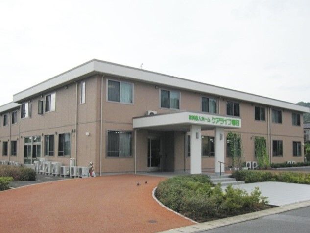 大きな車寄せが付いた２階建ての建物は横に長く、ベージュの外壁。玄関には手すり付きの階段もある。