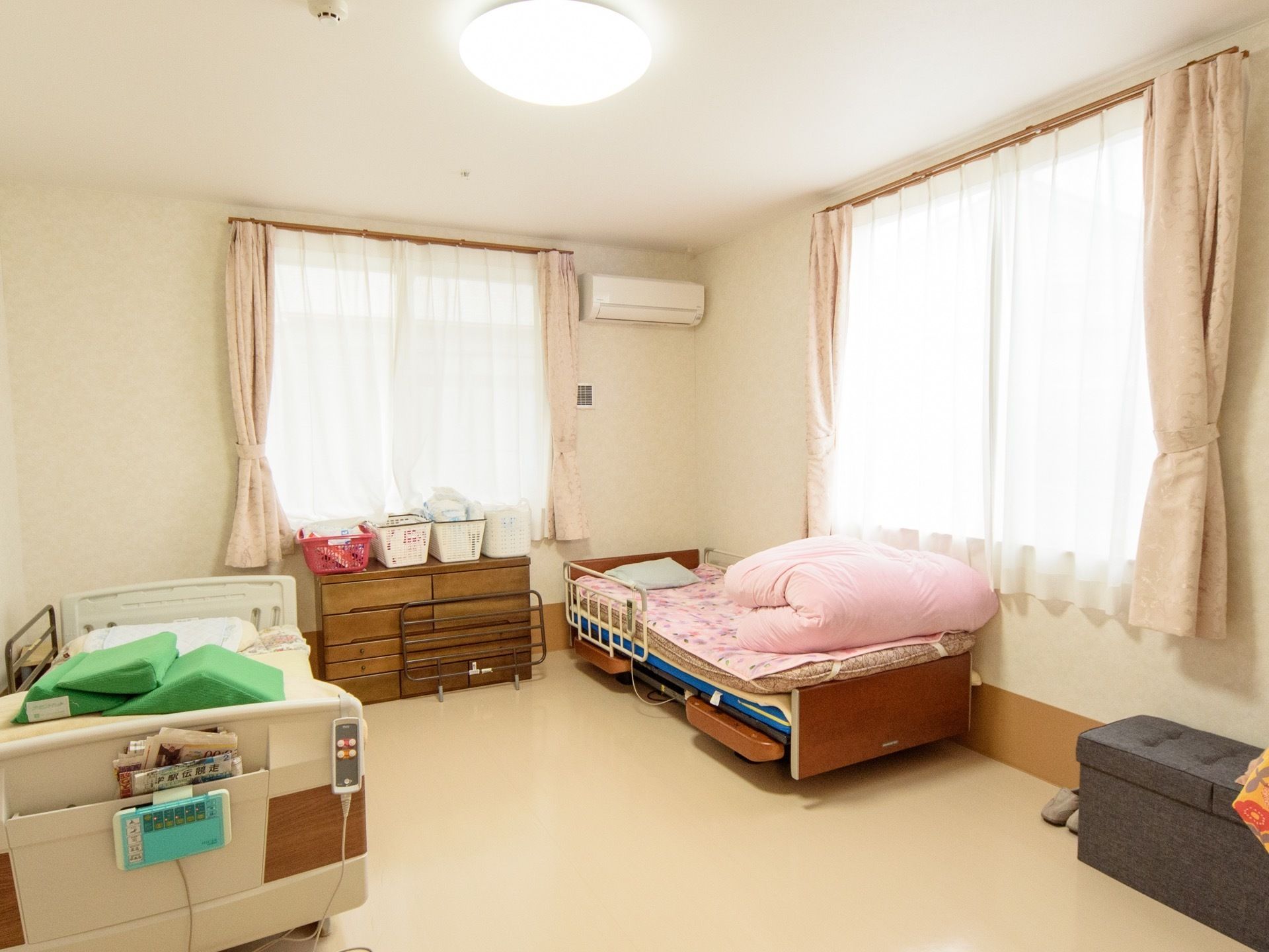 ２方向に窓がとられている居室。電動機能付きのベッドが２台設置されている。古民具風のチェストが窓際に置かれている。