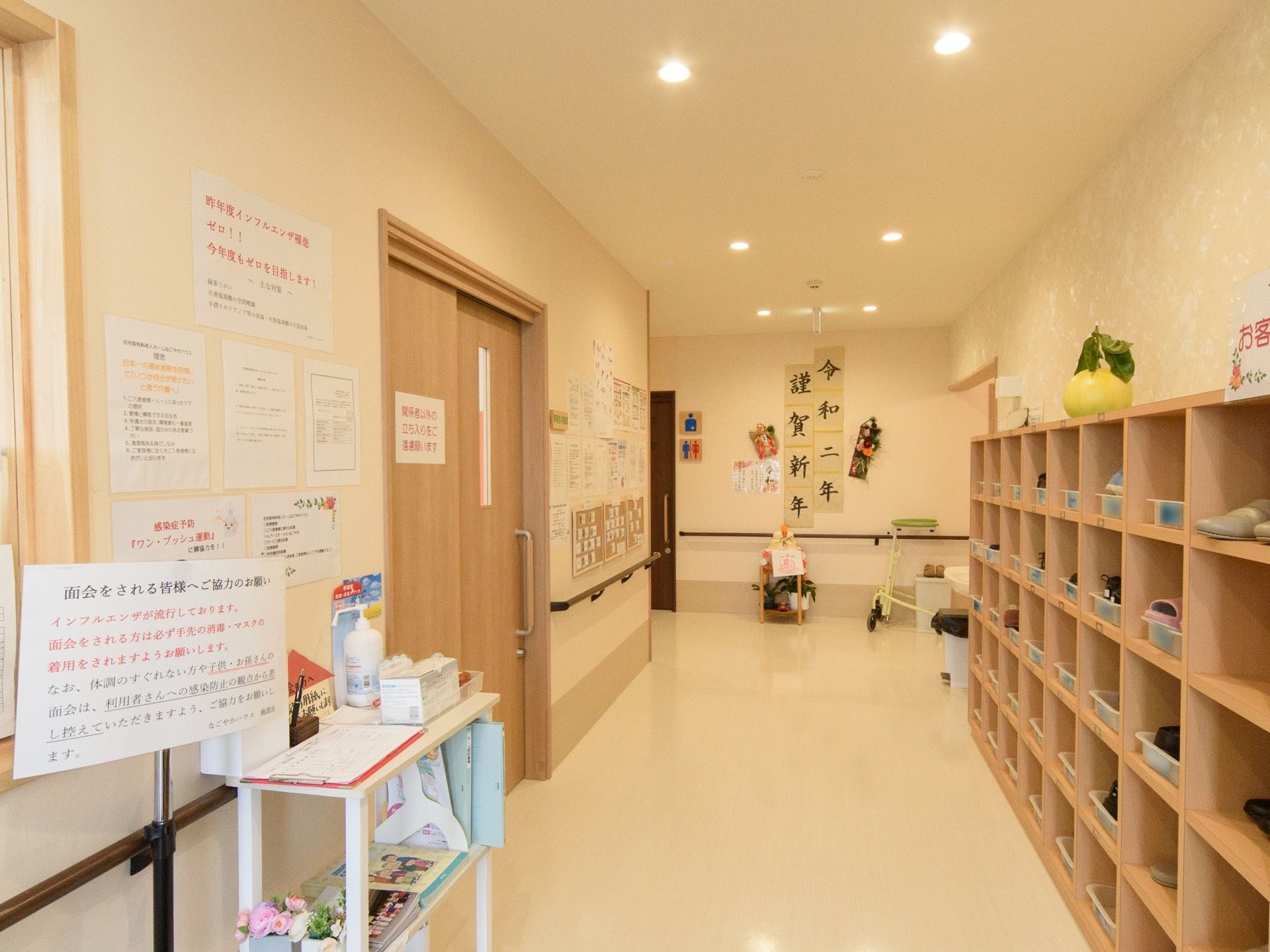右側に靴箱が並んでいる。左側に窓口があり、消毒用の液剤などが用意されている。突き当たりの壁には正月用の書が飾られている。