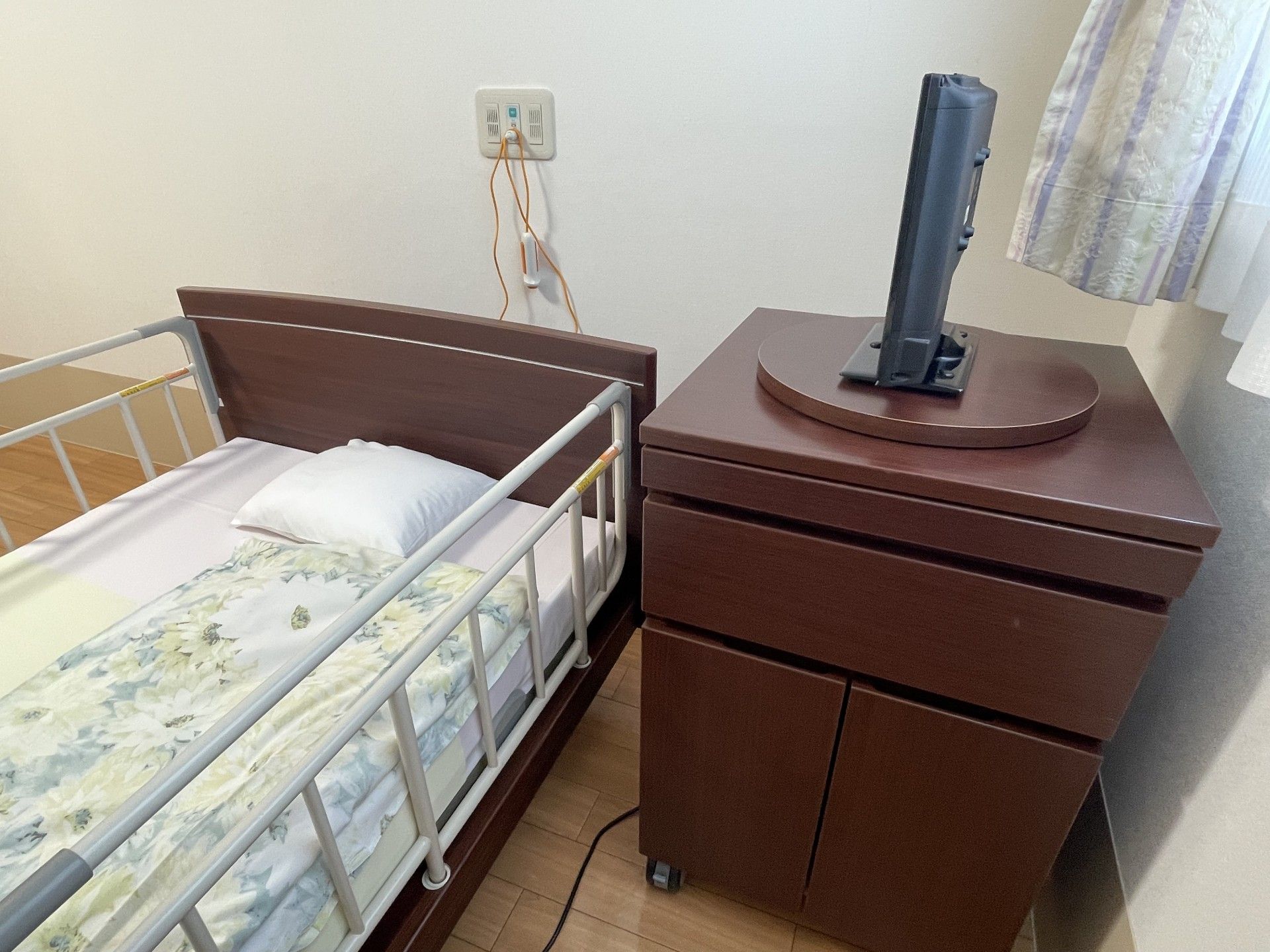 介護用ベッドとテレビ、2脚の椅子と洗面台がある個室