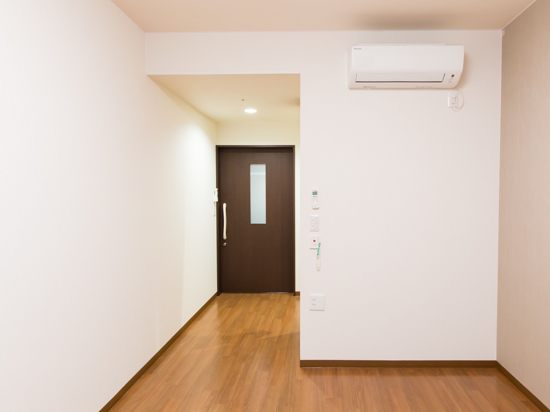 左奥に短い廊下が伸び、突き当たりにダークブラウンの板材の引き戸扉がある。扉には細長い窓がある。床はフローリングになっている。