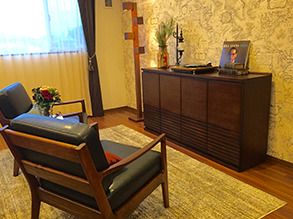 植物や本が飾られている収納家具やいす、花が飾られたテーブルが置かれている部屋。