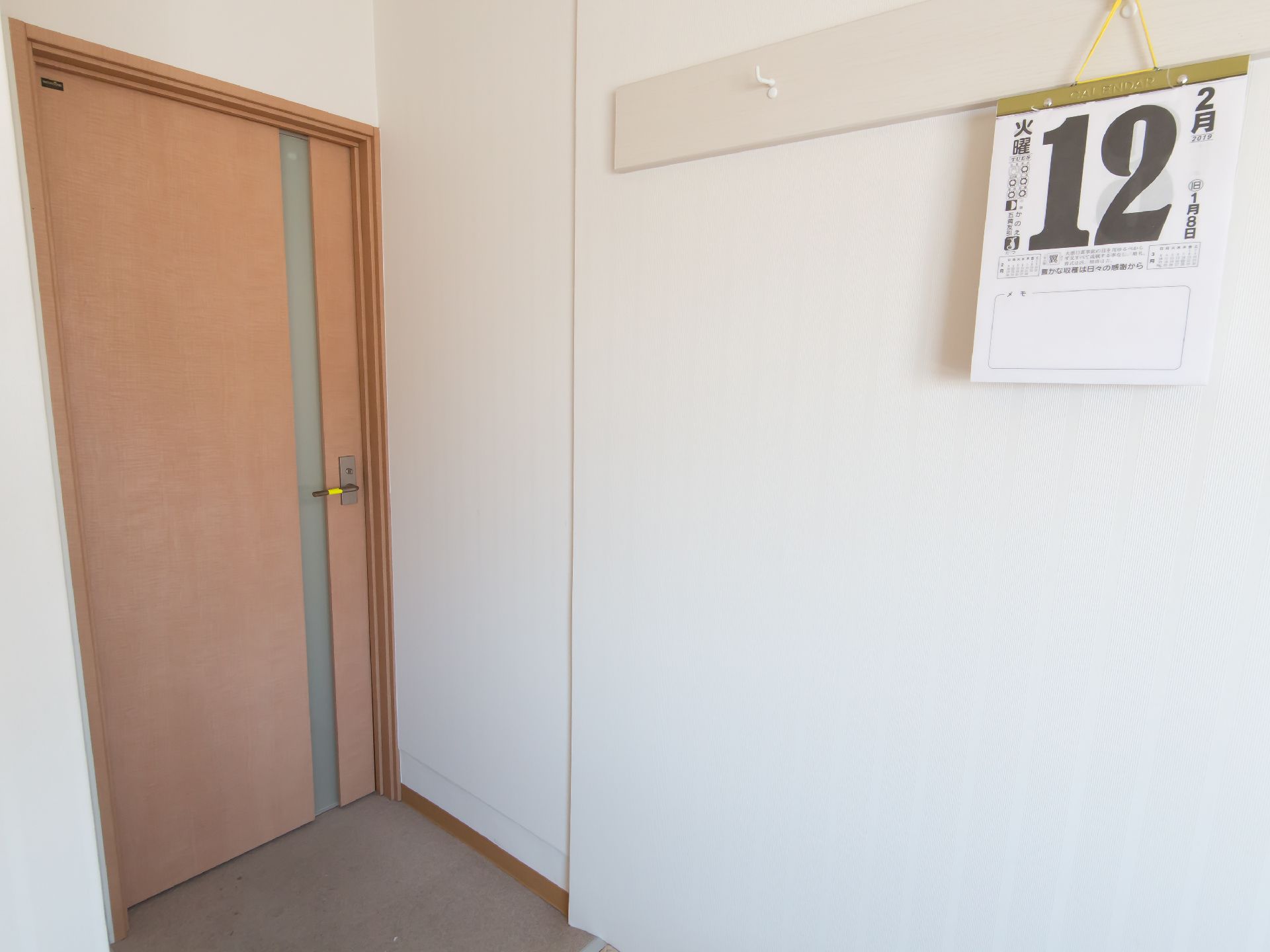 白を基調とした清潔感ある居室である。壁にはハンガー掛けが取りつけられており、カレンダーが掛けられている。