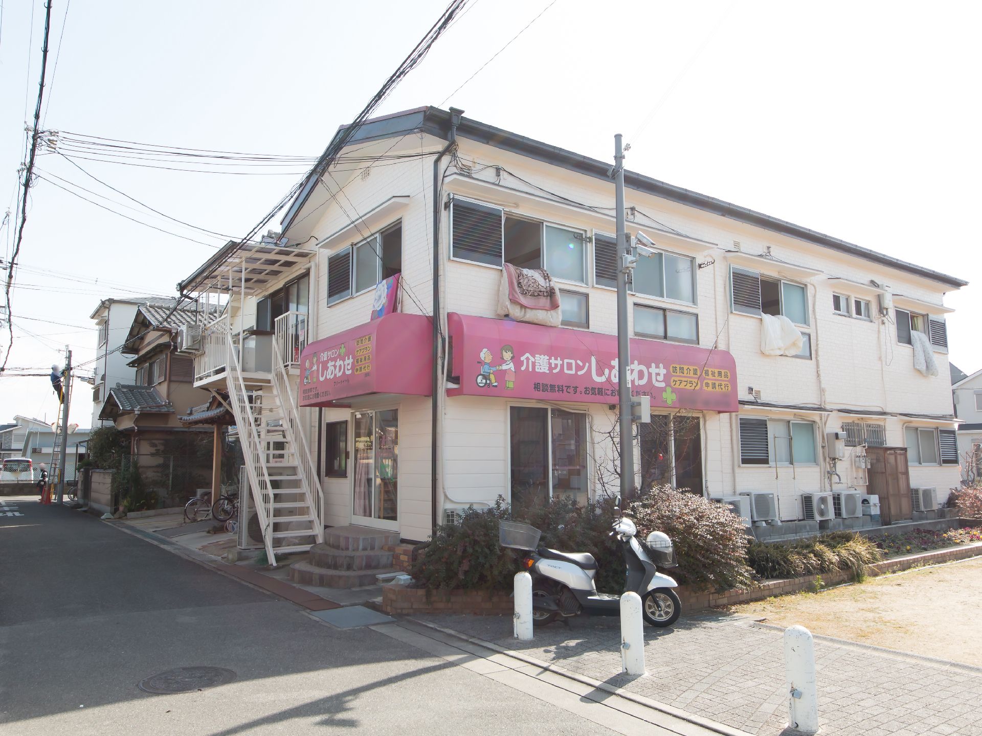 介護サロンが入っている建物。外壁に沿って複数のエアコンの室外機が設置されており、２階の居室の窓には布団が干されている。