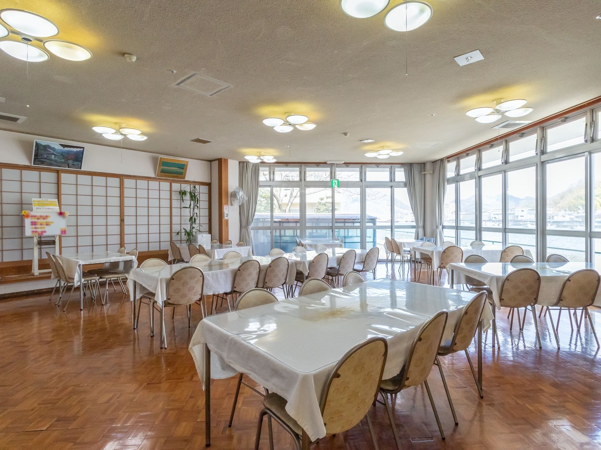明るく開放的な食堂である。壁一面に掃き出し窓がたくさん並んでおり、外の景色が良く見ることができる。反対側には障子が並んでいる。