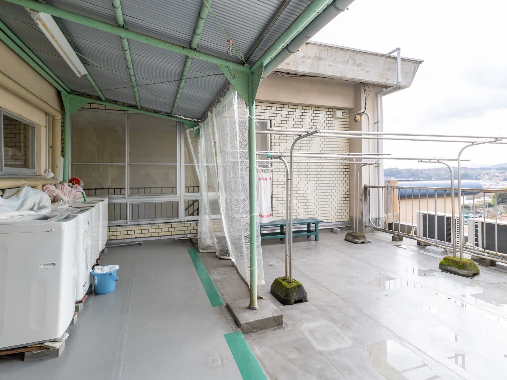 広いベランダに屋根が設置されており、その下に複数の洗濯機が並んでいる。隣接するように物干し場がある。