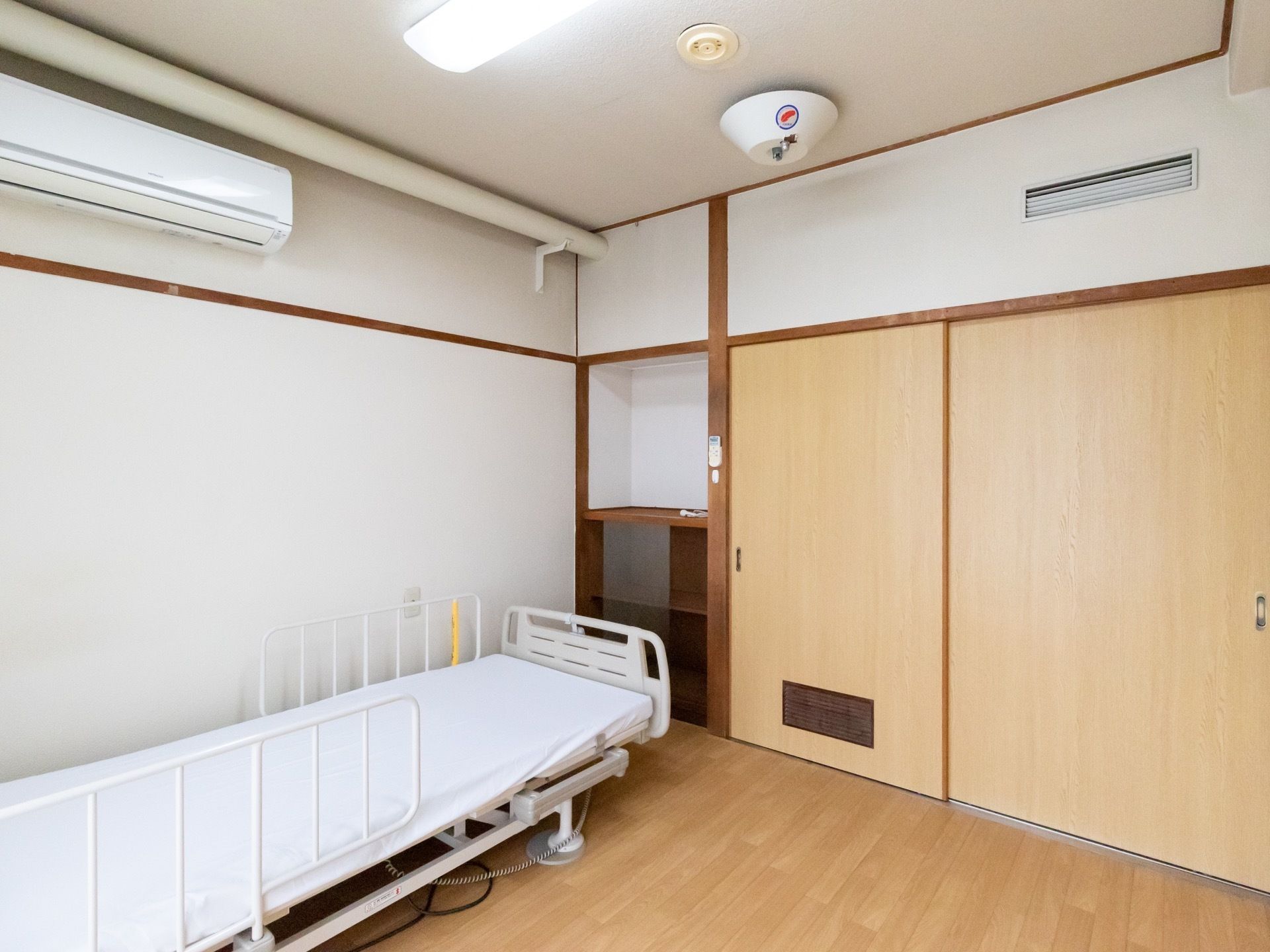 白地の壁と木製の柱が和風の印象を与える個室である。電動式の介護ベッドとエアコンが備えつけられている。
