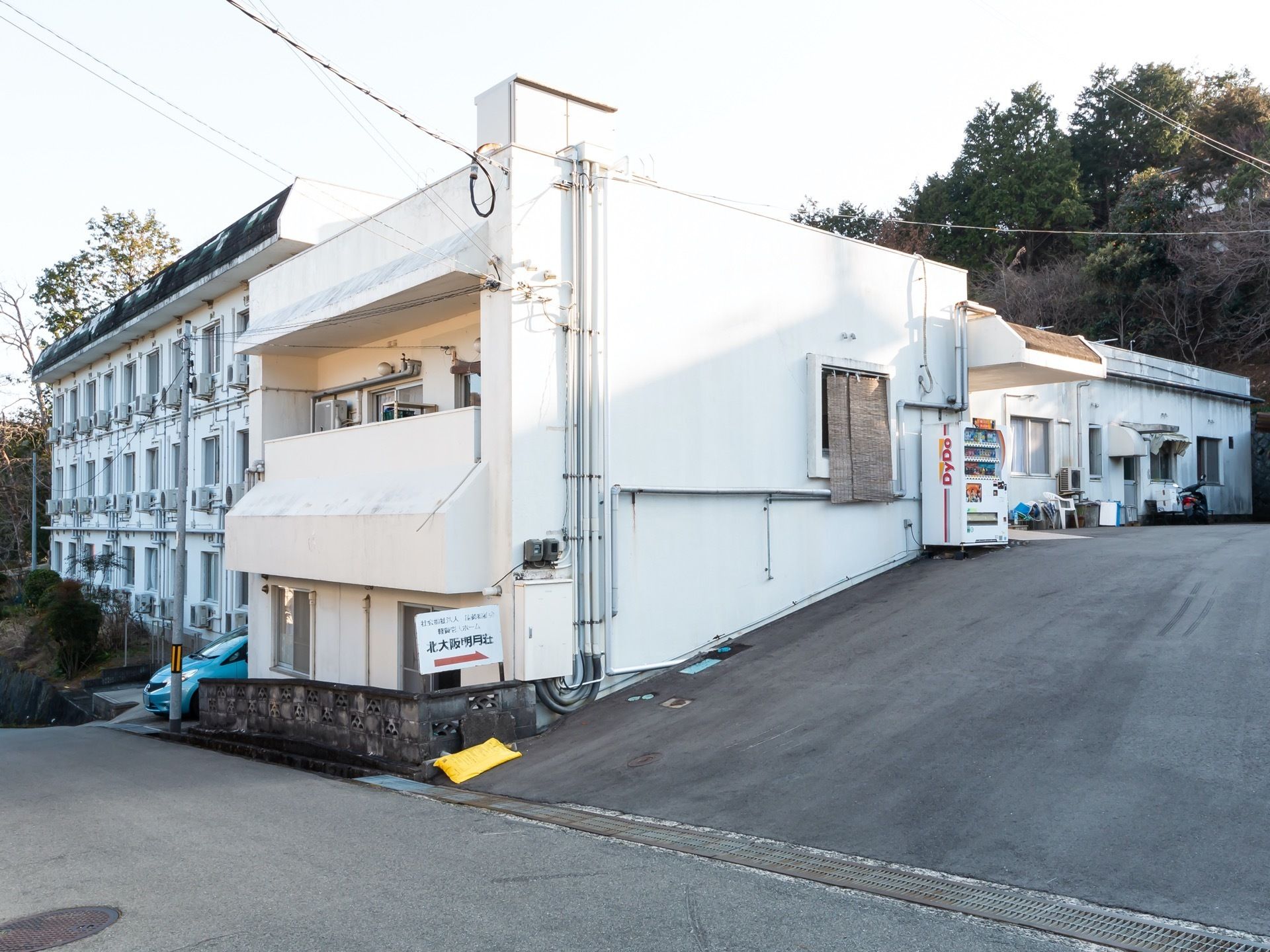 施設は白い３階建ての建物である。建物前に駐車スペースが設けられている。緩い傾斜が付いた玄関アプローチには、自販機が設置されている。