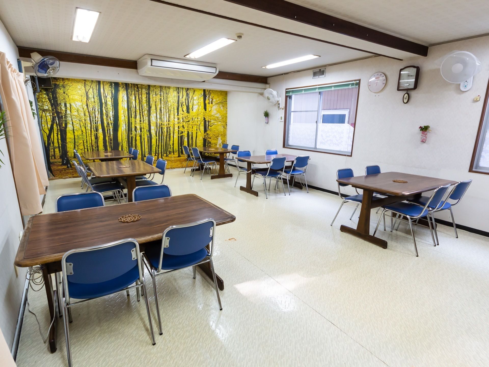 空間にゆとりを持たせた食堂である。椅子がセットされたテーブルが配置されている。壁には、ロールスクリーンや扇風機が設置されている。
