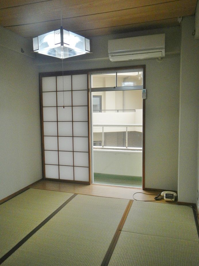 畳敷きの和室は日当たりがよく明るい。ベランダやエアコンもあり、窓の外にはベージュの建物もある。