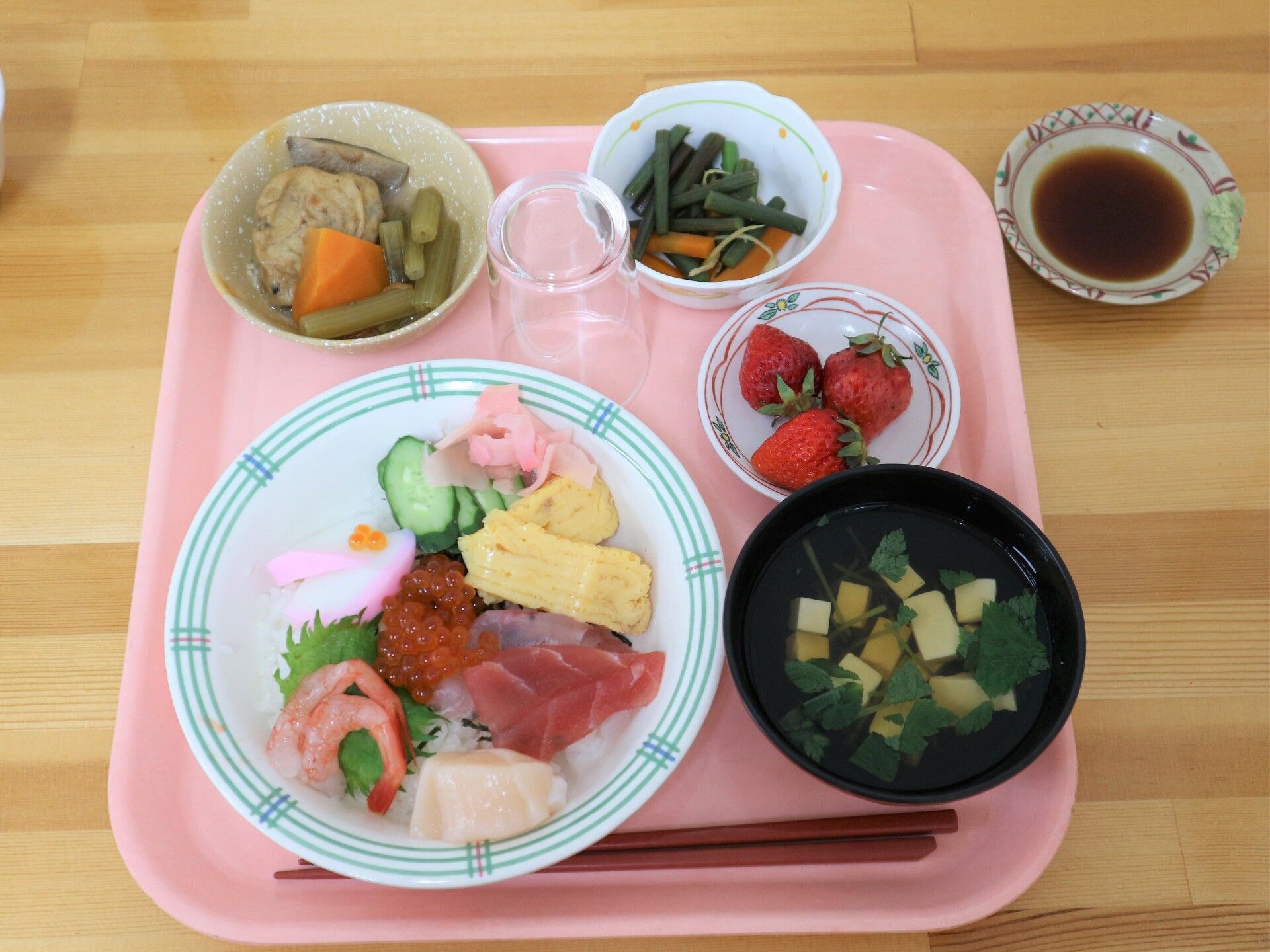 正方形のピンク色のトレイに配膳されたちらし寿司や煮物