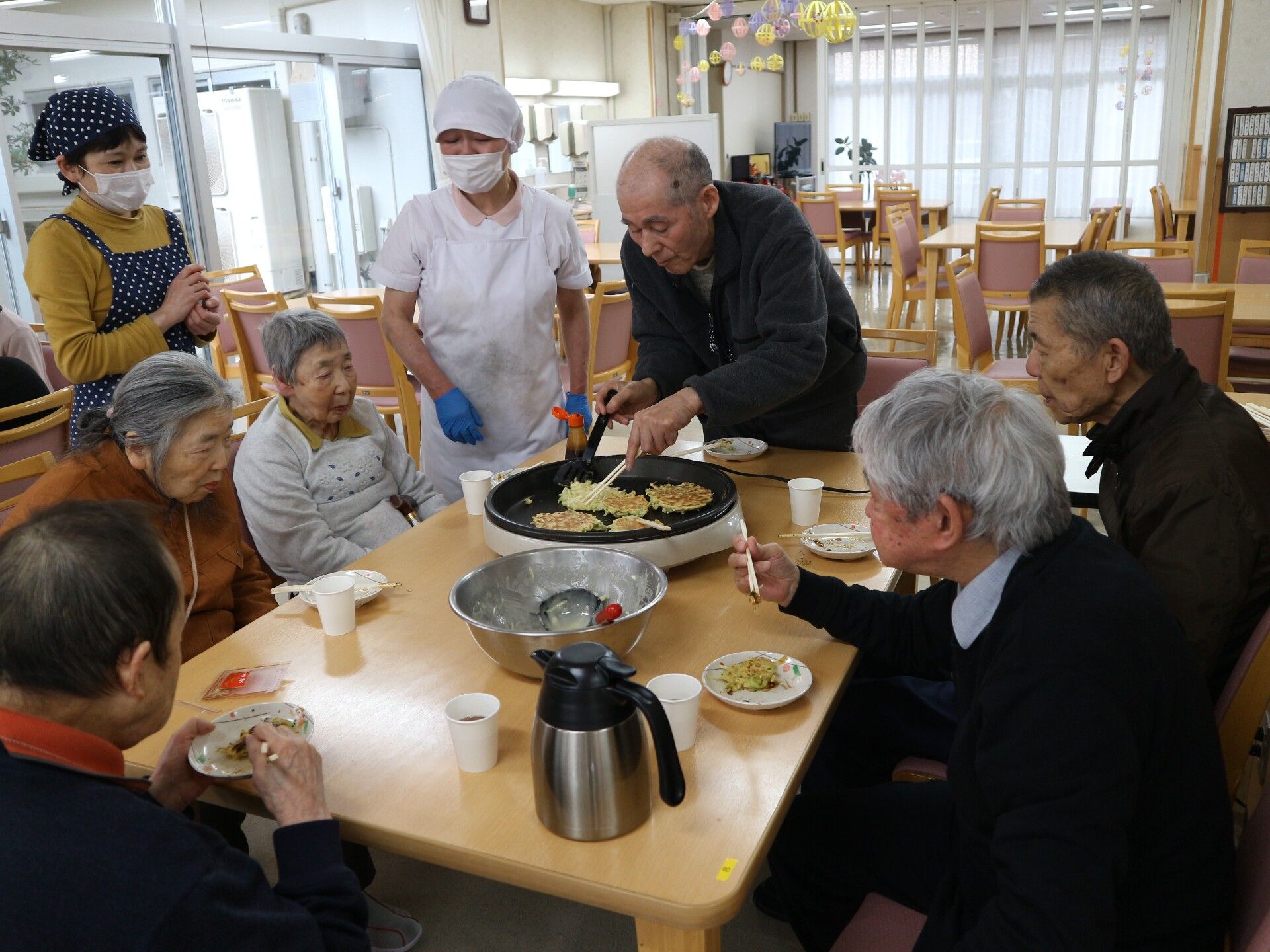 ホットプレートでお好み焼きを焼いているスタッフと入居者様