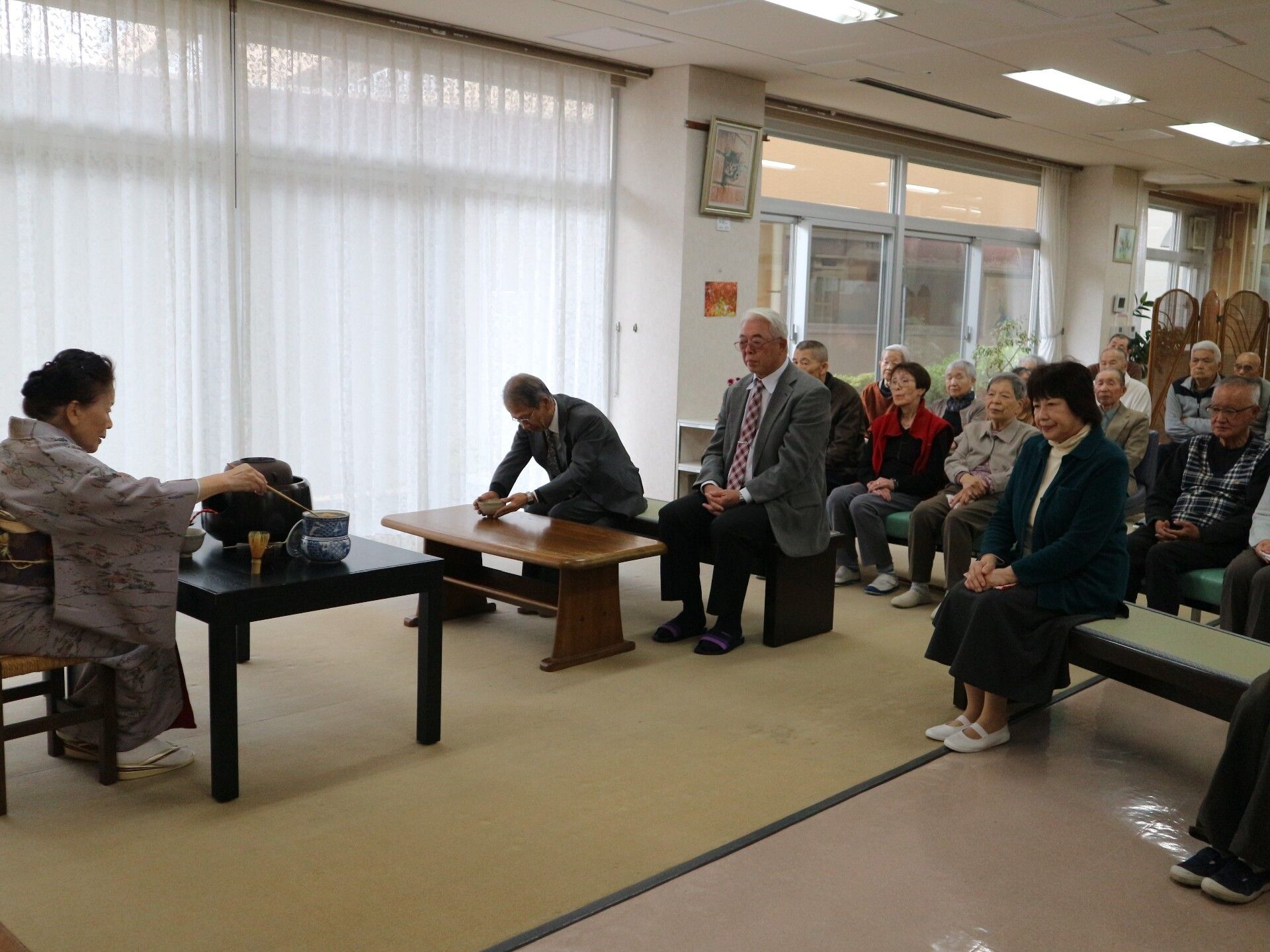 長椅子に座って、講師が作るお茶の様子を見ている入居者様