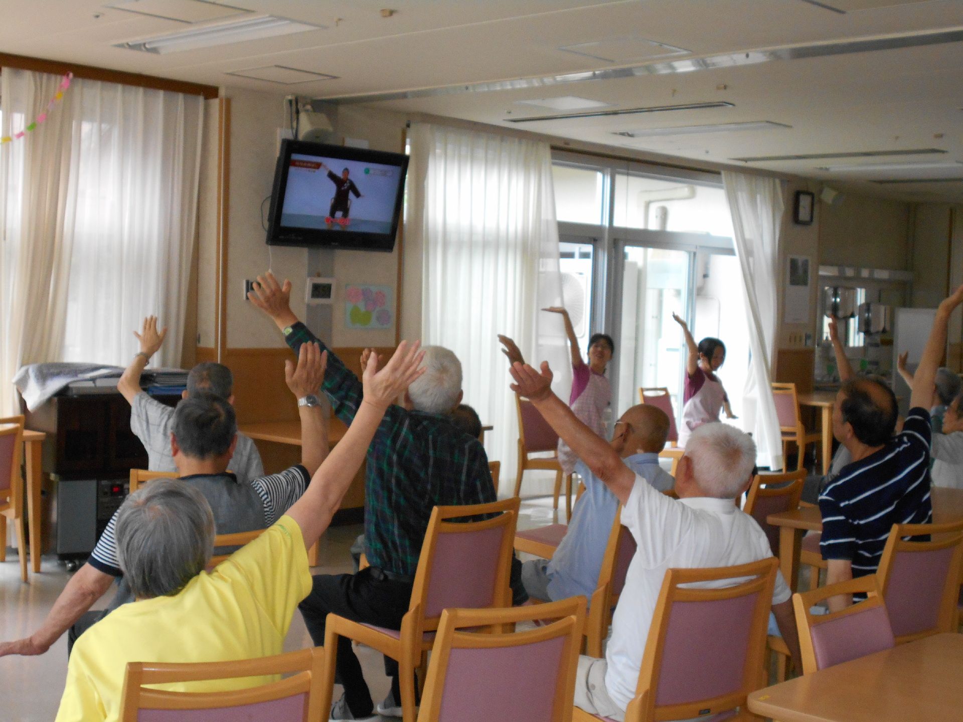 壁に取り付けられたテレビで流れる体操を一緒にする入居者様