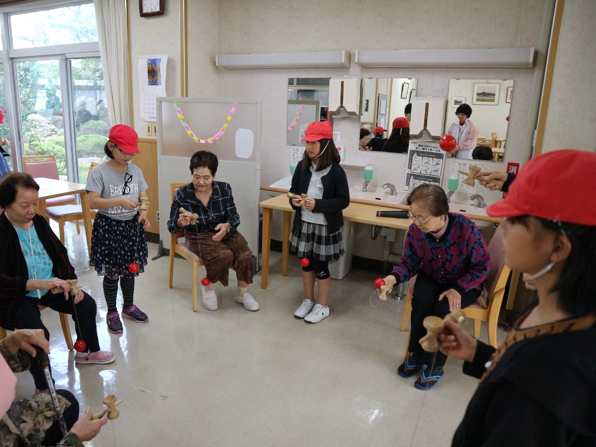紅白帽をかぶった近所の子供たちと一緒にけん玉で遊んでいる入居者様