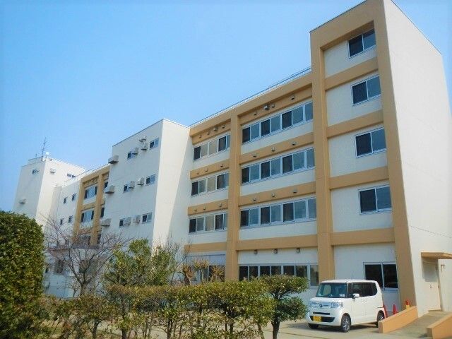 植え込みや樹木で囲まれている、４階建ての白とオレンジの建物