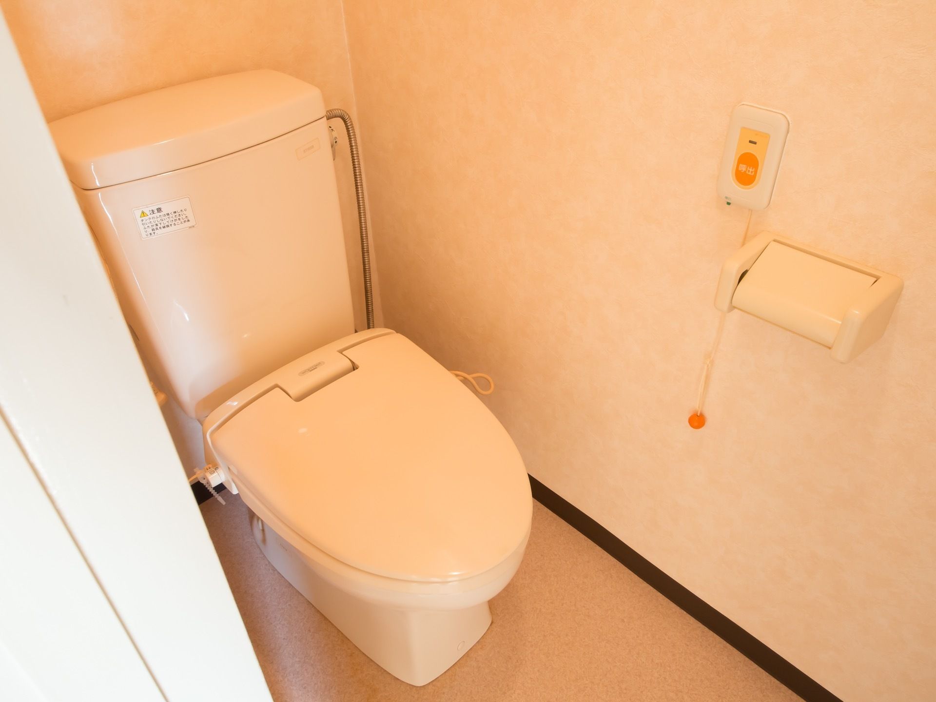 白くて清潔感のある便座が設置されている。壁にはトイレットペーパーホルダーや、呼び出しボタンが取りつけられている。