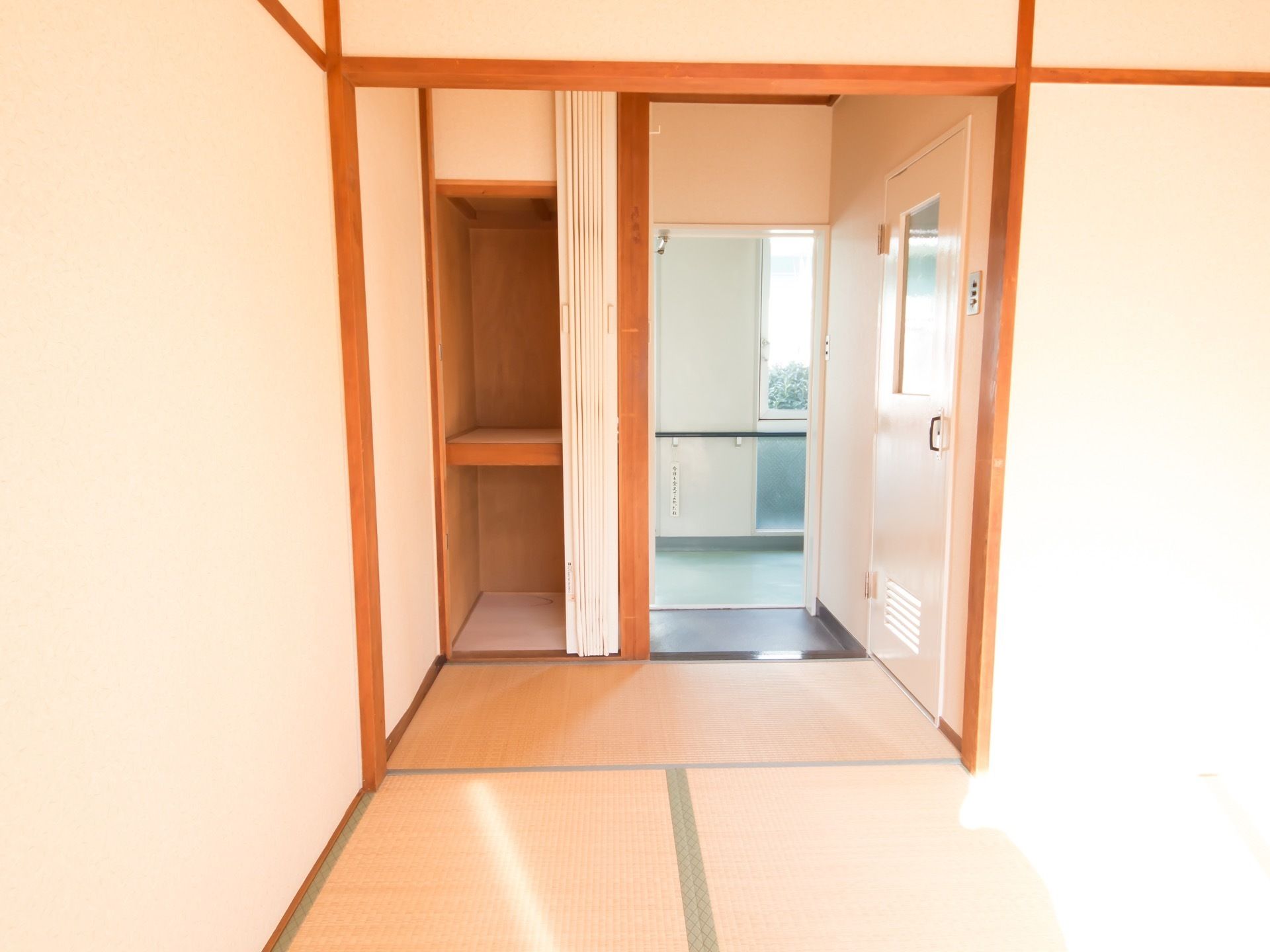 畳の部屋になっており、入り口のドアが開いている。入口の側には押し入れがあり、白いアコーディオンカーテンがつけられている。