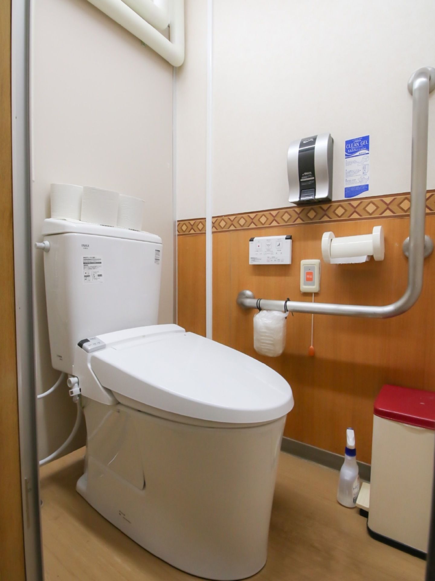 温水洗浄機能付きの洋式トイレのある個室で、壁には緊急コールやリモコン、便座用の消毒液が設置されている。