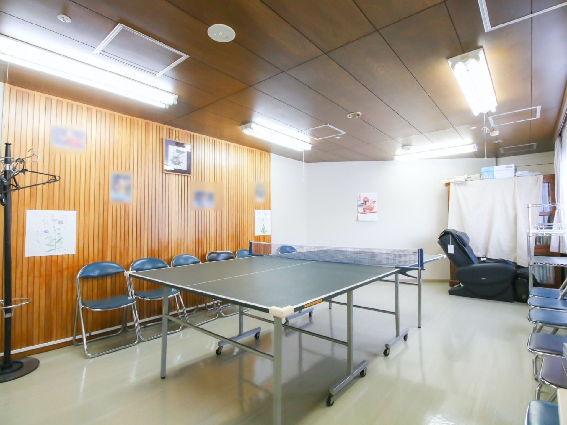 一部の壁が、木製の格子状になった部屋で、真ん中に卓球台が置かれている。部屋の奥に、黒い革張りのマッサージチェアが一台ある。