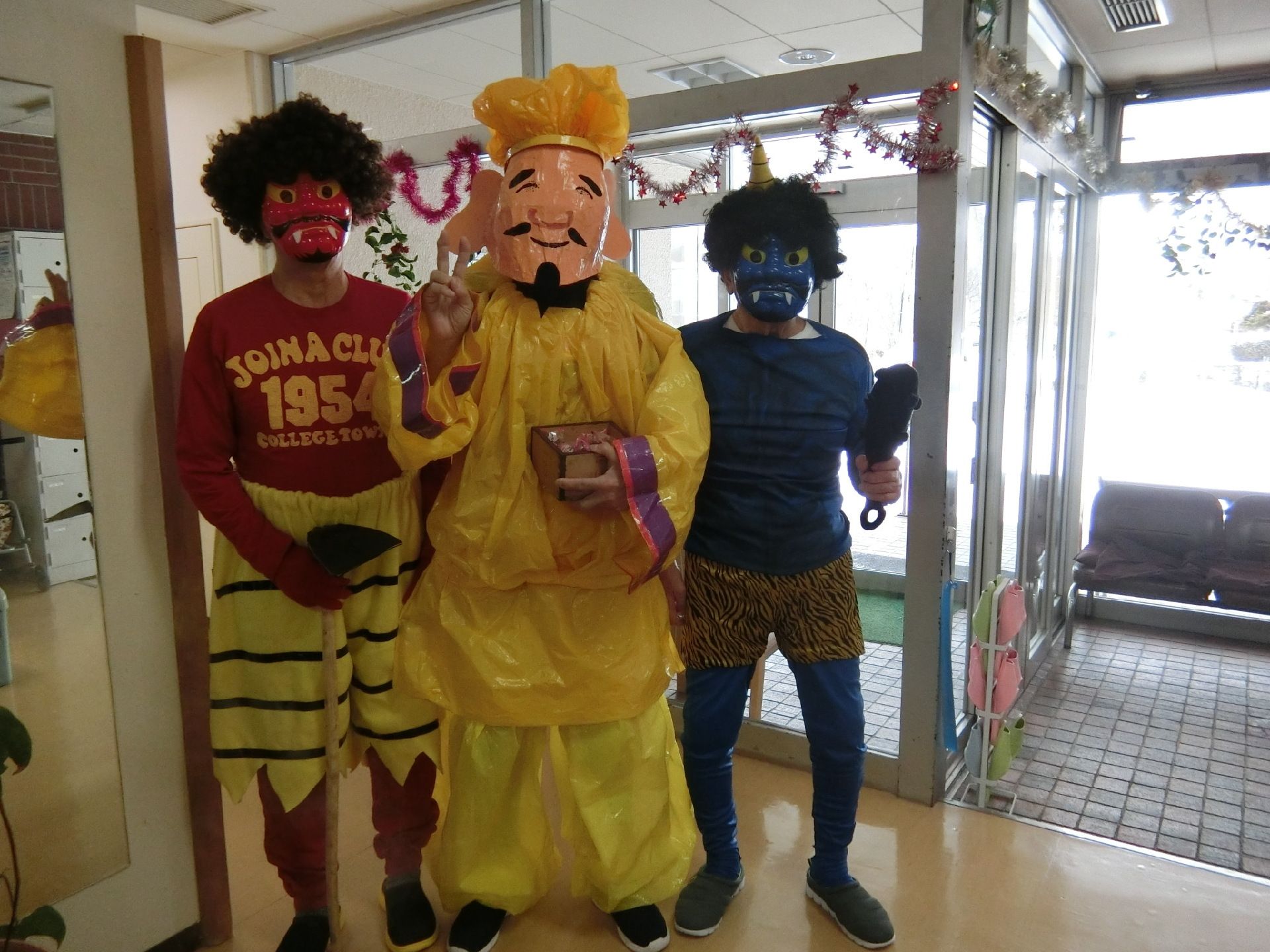 赤鬼や青鬼に仮装したスタッフに囲まれて、黄色い服を着て福の神のお面をかぶったスタッフが立っている。鬼は小さな金棒も持っている。