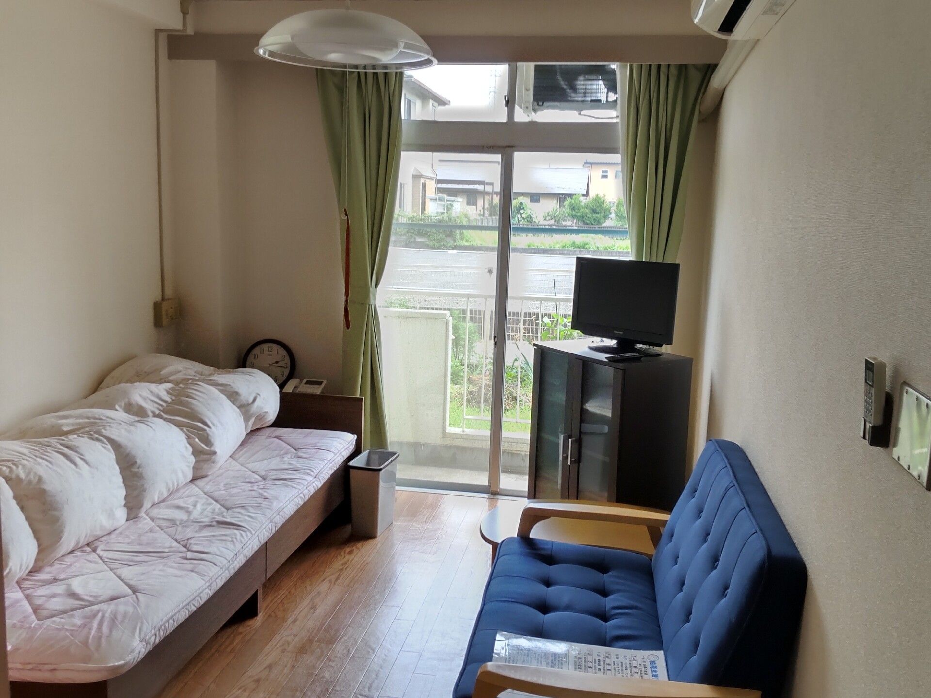 ブルーのソファや寝具付きのベッド、テレビが置かれたフローリングの部屋には大きな窓が付いている。