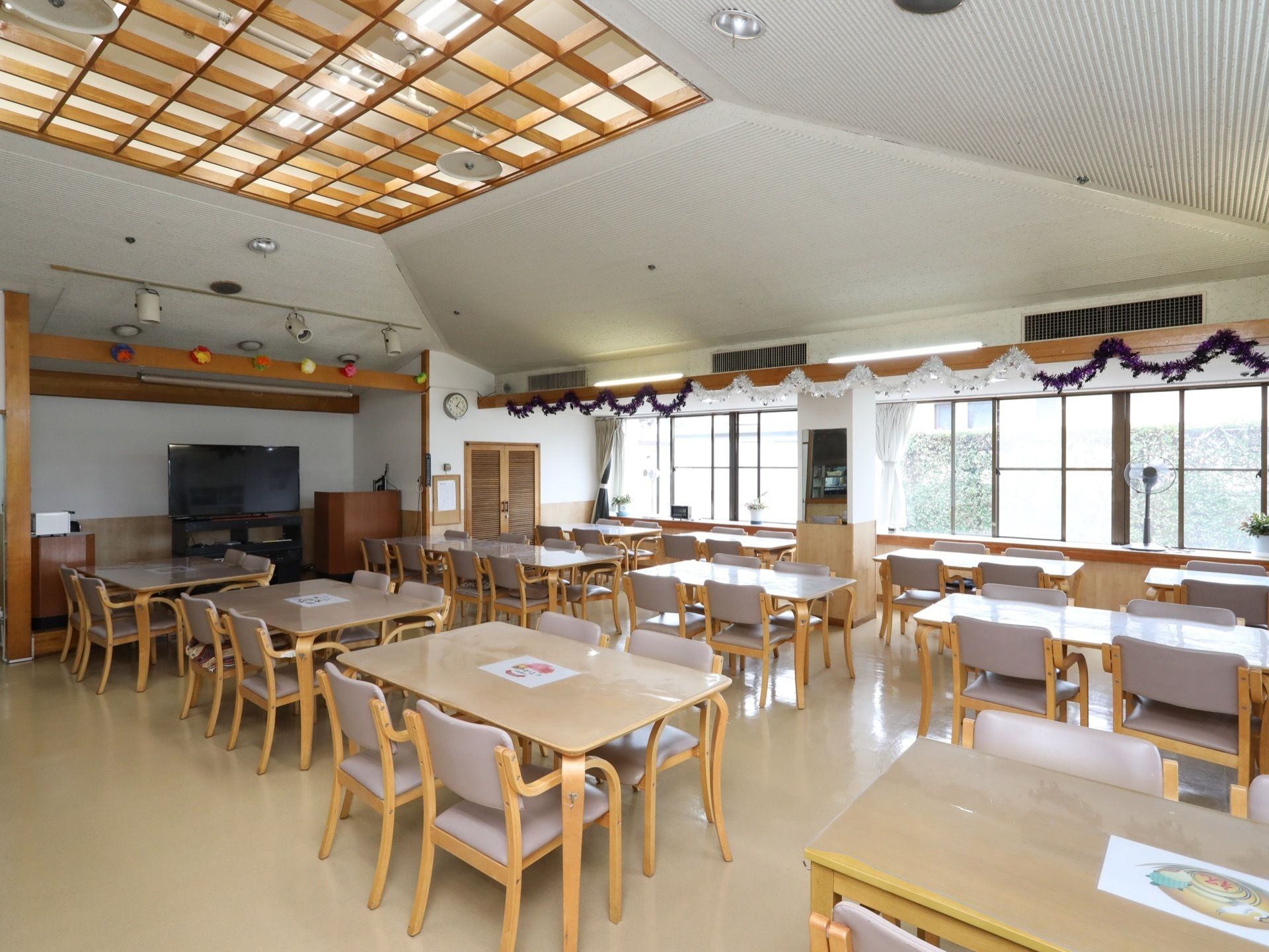 食堂の天井は木の格子状になっている。奥の壁際に大画面テレビが置かれ、その手前の天井にはスポットライトがかかっている。