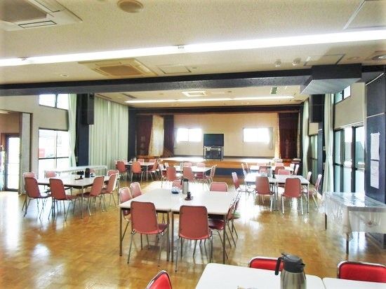 白い四角いテーブルに赤い椅子がセットされた食堂。大きな窓がたくさんつき明るい雰囲気。