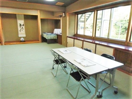 娯楽室には手前にパイプ椅子が４脚セットされた長テーブルがあり、奥には掛け軸がかけられた床の間がある。