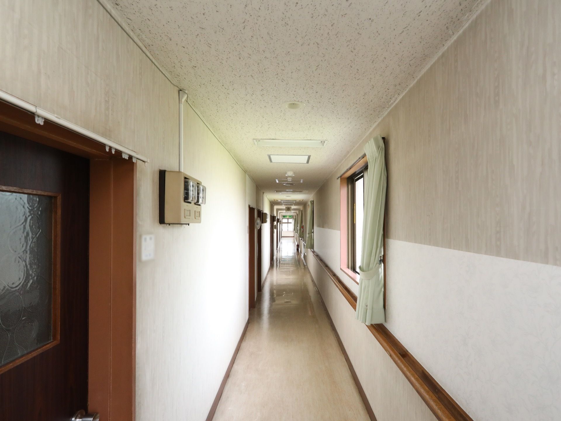 通路の突き当たりに非常口がある。左側の壁面には扉があり、右側の壁面には窓や木製の手すりがある。
