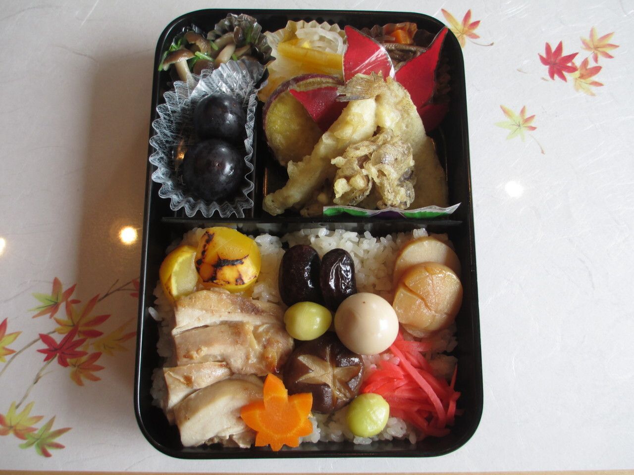天ぷらや黒豆、チキンや酢の物、栗ご飯とデザートのぶどうが入った弁当